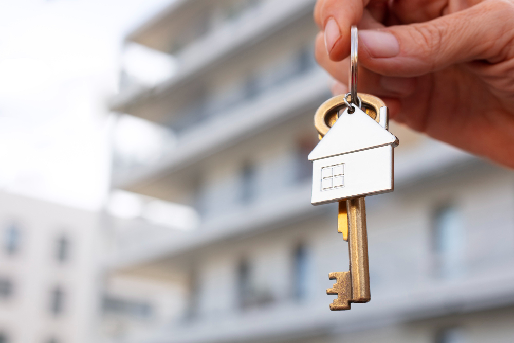 Mão segura chave de casa em frente a condomínio