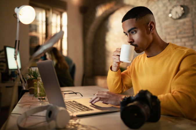 Jovem empresário negro bebendo café enquanto trabalhava até tarde em um computador no escritório