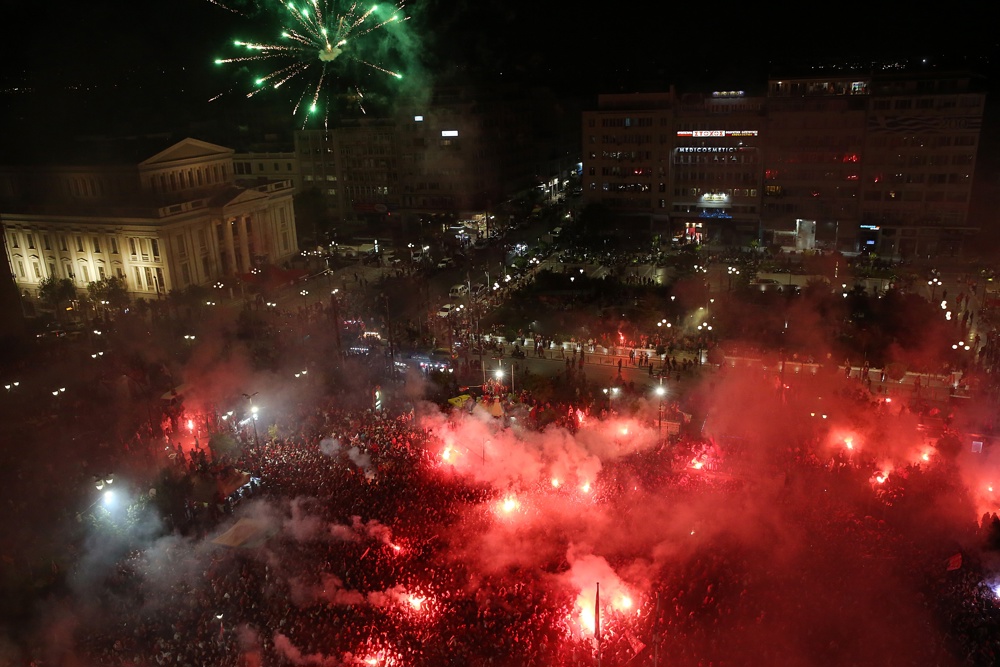 Os adeptos do Olympiacos acendem foguetes e fogos de artifício enquanto assistem à transmissão pública do jogo final da UEFA Europa Conference