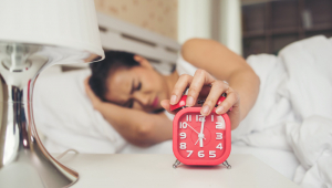 Mão de mulher segurando o despertador na cama