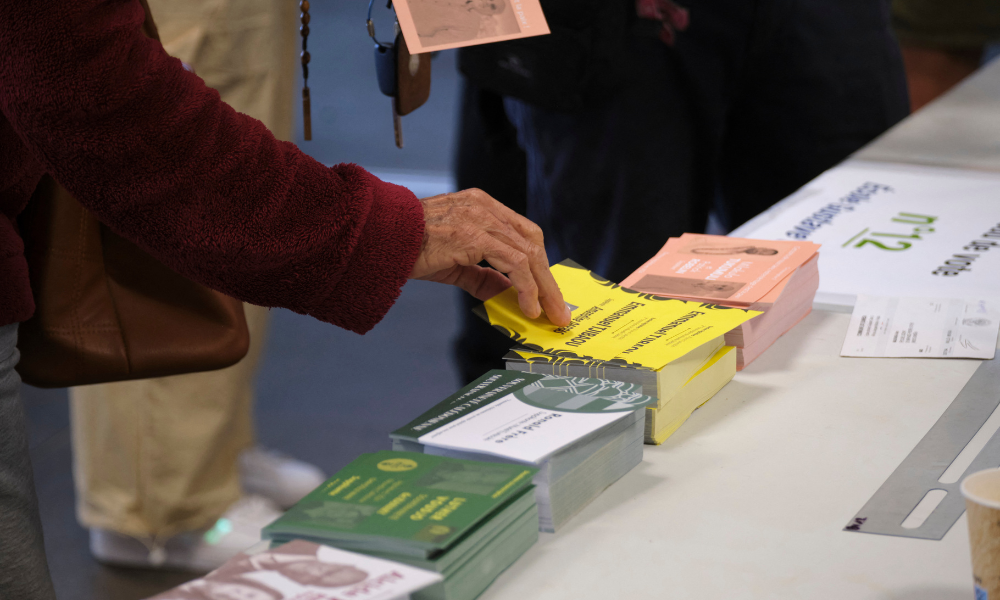 Uma pessoa recolhe cédulas em uma seção eleitoral dentro da prefeitura de Koutio antes de votar durante o primeiro turno das eleições legislativas da França em Dumbea, no segundo distrito eleitoral do território francês do Pacífico, na Nova Caledônia, em 30 de junho