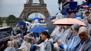 s espectadores usam capas de chuva e sentam-se sob seus guarda-chuvas enquanto aguardam o início da Cerimônia de Abertura dos Jogos Olímpicos de Paris 2024
