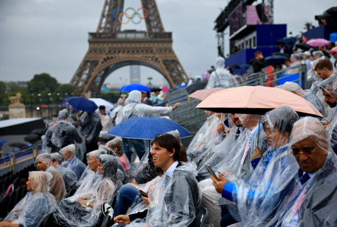 s espectadores usam capas de chuva e sentam-se sob seus guarda-chuvas enquanto aguardam o início da Cerimônia de Abertura dos Jogos Olímpicos de Paris 2024