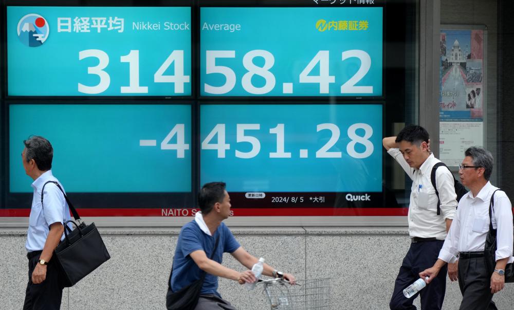 Pedestres passam por uma exibição mostrando as informações de fechamento do Índice Nikkei, que registrou a maior perda da história em Tóquio