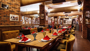 Uma sala de restaurante com paredes de tijolo vermelho, mesas de madeira e canos no teto