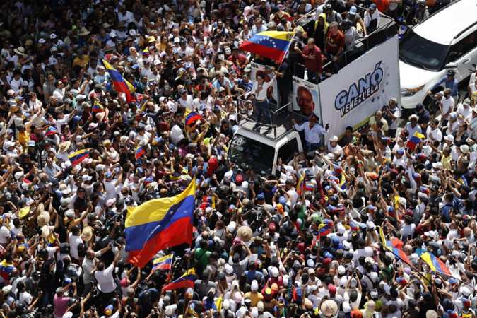 A líder da oposição venezuelana María Corina Machado (c) agita a bandeira da Venezuela diante de seguidores