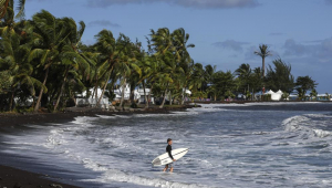 Um homem segura uma prancha de surfe perto do local das competições de surfe dos Jogos Olímpicos de Paris 2024 em Teahupo'o