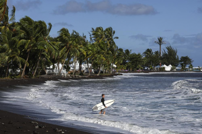 Um homem segura uma prancha de surfe perto do local das competições de surfe dos Jogos Olímpicos de Paris 2024 em Teahupo'o