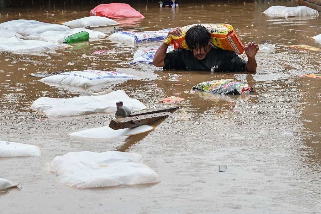 A man carrying a sack of flour wades through flood waters after the Bagmati River overflowed following heavy monsoon rains in Kathmandu on September 28, 2024. Floods and landslides caused by heavy downpours in Nepal killed at least 10 people across the Himalayan country, with rescue teams searching for 18 missing, a disaster official said on September 28.