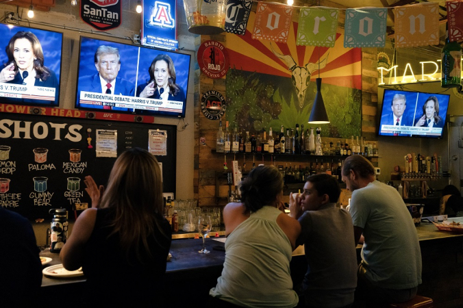 Pessoas sentam-se atrás de um bar enquanto participam de uma festa para assistir ao debate presidencial dos EUA entre a vice-presidente e candidata presidencial democrata Kamala Harris e o ex-presidente dos EUA e candidato presidencial republicano Donald Trump, no American Eat Co. em Tucson, Arizona