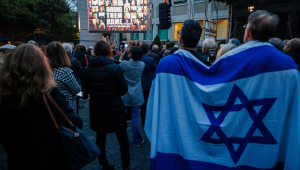 Participantes com bandeira de Israel enrolada nos ombros assistem a uma projeção de vídeo sobre os eventos de 7 de outubro durante um evento que relembra o ataque a Israel em 7 de outubro