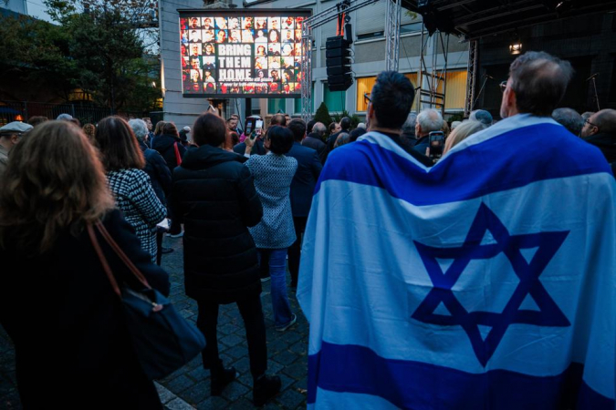 Participantes com bandeira de Israel enrolada nos ombros assistem a uma projeção de vídeo sobre os eventos de 7 de outubro durante um evento que relembra o ataque a Israel em 7 de outubro