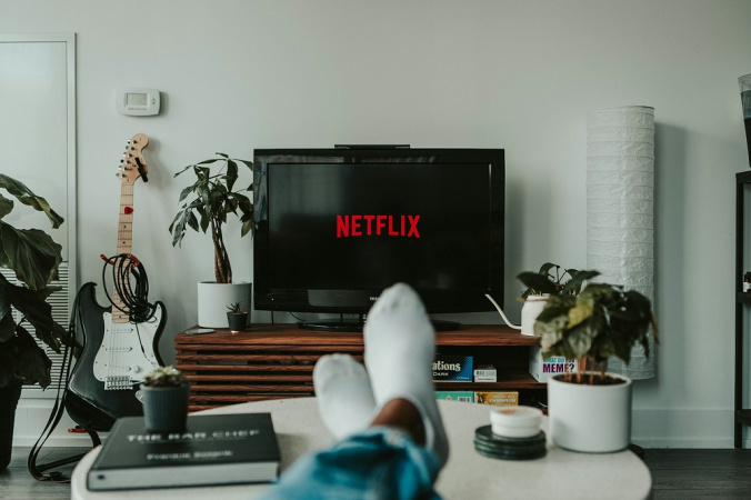 Homem com os pés esticados, de meia, vê Netflix