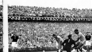 O brasileiro Djalma Santos (e) retira a bola das mãos do goleiro húngaro Grosits Gyula para colocar na marca do pênalti enquanto Didi (c) permanece caído durante partida entre Brasil e Hungria na Copa do Mundo de Futebol de 1954, disputada em Berna, na Suíça. A Hungria venceu a partida por 4a 2. Durante este jogo três jogadores foram expulsos pelo árbitro britânico Arthur Ellis e depois do jogo houve confrontos entre as equipes no caminho para o vestiário.