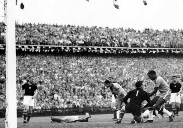 O brasileiro Djalma Santos (e) retira a bola das mãos do goleiro húngaro Grosits Gyula para colocar na marca do pênalti enquanto Didi (c) permanece caído durante partida entre Brasil e Hungria na Copa do Mundo de Futebol de 1954, disputada em Berna, na Suíça. A Hungria venceu a partida por 4a 2. Durante este jogo três jogadores foram expulsos pelo árbitro britânico Arthur Ellis e depois do jogo houve confrontos entre as equipes no caminho para o vestiário.