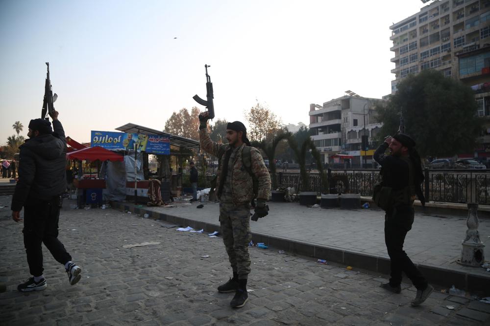 Combatentes da oposição disparam suas armas para o alto em celebração após entrarem na cidade de Hama, na Síria