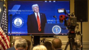 Membros da mídia acompanham em uma tela de TV o discurso do presidente dos Estados Unidos, Donald J. Trump, transmitido da sala de imprensa durante a Conferência Republicana de 2025 no resort Trump National Doral, em Miami, Flórida