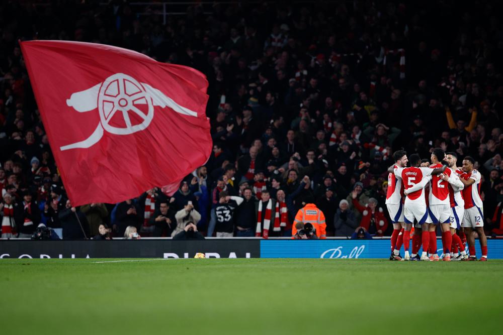 Jogadores do Arsenal comemoram o quinto gol da equipe enquanto torcedores agitam uma bandeira do clube