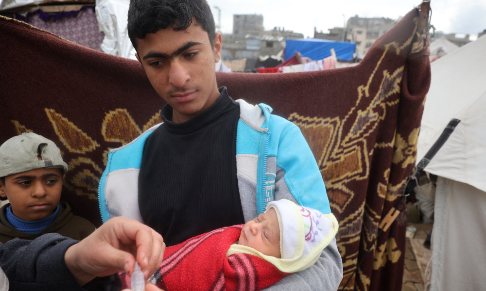 Palestinian man holds a baby as a medic prepares to administer a polio vaccine at a camp for displaced people in Nuseirat in the central Gaza Strip on February 23, 2025, a day after the third mass polio vaccination campaign began in Gaza