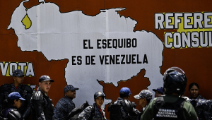 Integrantes da Polícia Nacional Bolivariana e da Guarda Nacional estão ao lado de um mural com o mapa da Venezuela e a frase "O Essequibo pertence à Venezuela" durante um protesto do Dia do Trabalhador em Caracas