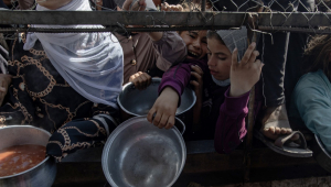 Palestinos deslocados internamente aguardam do lado de fora de uma cozinha comunitária para receber porções limitadas de alimento, em meio à escassez de comida, em Khan Younis, sul da Faixa de Gaza,