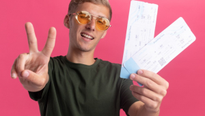 Jovem bonito sorridente, vestindo uma camisa verde e óculos, segurando ingressos