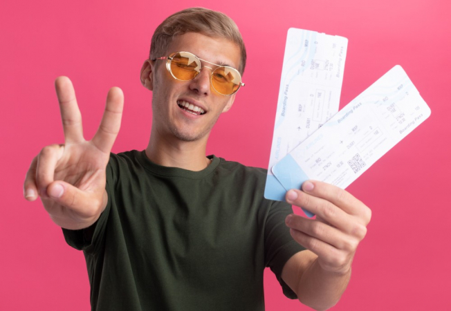 Jovem bonito sorridente, vestindo uma camisa verde e óculos, segurando ingressos