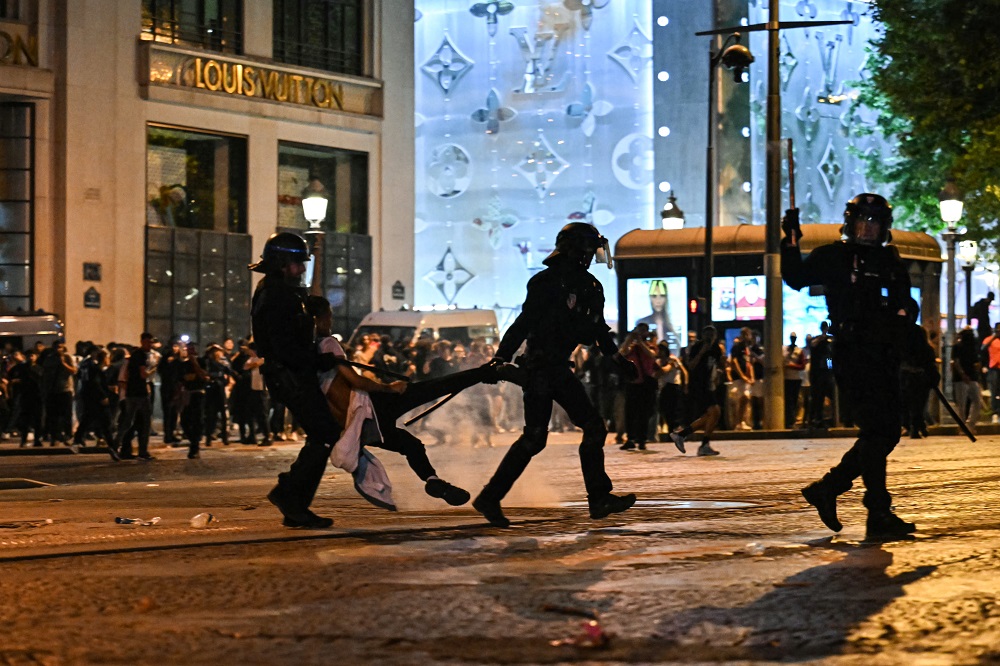 Policiais de choque detêm uma pessoa enquanto torcedores do Paris Saint-Germain comemoram a vitória do PSG na final da Liga dos Campeões da UEFA