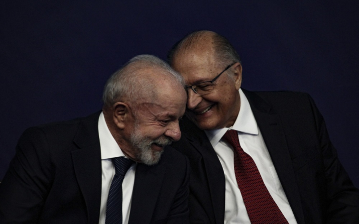 Geraldo Alckmin conta algo para Lula ao pé do ouvido; ambos estão rindo