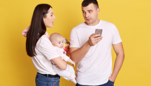 Jovem mãe furiosa segurando o bebê nas mãos e olhando para o marido usando o telefone