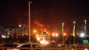 Pessoas dirigem enquanto fogo e fumaça se elevam de um depósito de petróleo em Teerã, no Irã