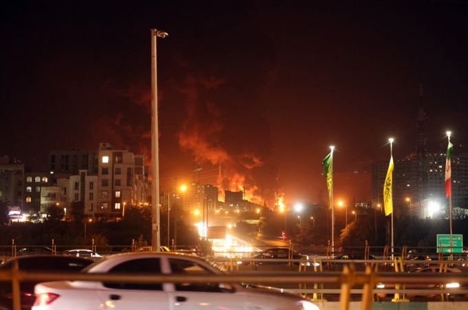 Pessoas dirigem enquanto fogo e fumaça se elevam de um depósito de petróleo em Teerã, no Irã