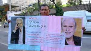 Fã segura um cartaz e faz homenagem em frente ao local onde o ator Francisco Cuoco está sendo velado no bairro da Bela Vista