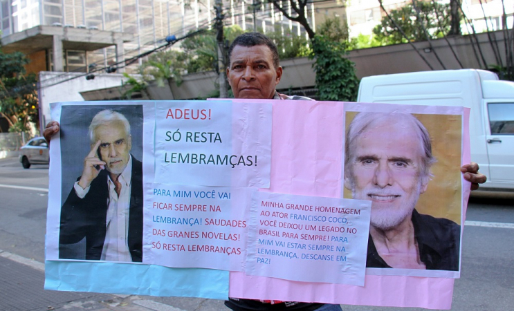 Fã segura um cartaz e faz homenagem em frente ao local onde o ator Francisco Cuoco está sendo velado no bairro da Bela Vista