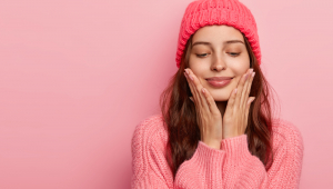 Foto de estúdio de uma modelo feminina de aparência agradável tocando o queixo com as palmas das mãos