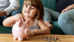 Menina coloca moedas em cofrinho em formato de porco