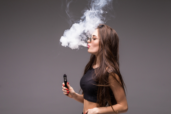 Jovem de óculos escuros e roupas pretas vaping e soprando fumaça