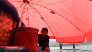 Vendedor ambulante se abriga sob o guarda-chuva de sua carroça durante a chuva em Srinagar, Índia