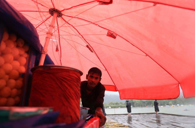 Vendedor ambulante se abriga sob o guarda-chuva de sua carroça durante a chuva em Srinagar, Índia
