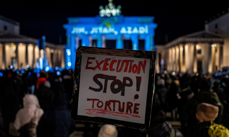 Uma ativista exibe um cartaz com as palavras "Parem a execução e a tortura", durante uma manifestação em apoio aos manifestantes no Irã, em frente ao Portão de Brandemburgo iluminado com as palavras "Mulher, Vida, Liberdade" em vários idiomas, incluindo curdo e persa, em Berlim, em 13 de dezembro de 2022. (Foto de John MACDOUGALL / AFP)