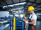 Operário de fábrica vestindo uniforme e capacete operando máquina industrial com joystick de botão na sala de produção