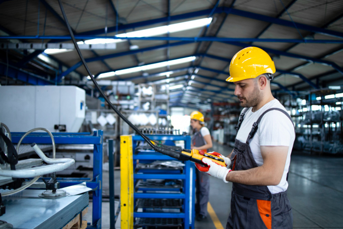 Operário de fábrica vestindo uniforme e capacete operando máquina industrial com joystick de botão na sala de produção