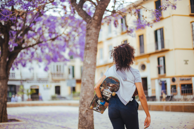 Menina segurando skate sob árvores