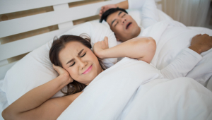 Mulher bloqueando as orelhas com homem dormindo roncando na cama