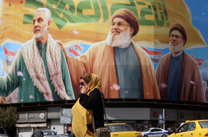 Mulher iraniana passa por um outdoor com imagens dos falecidos líderes do Hezbollah Hassan Nasrallah (C) e Sheikh Safieddine (D), junto ao falecido general do Corpo de Guardiões da Revolução Islâmica (IRGC) e comandante da Força Quds, Qasem Soleimani (E)
