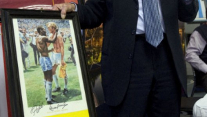 Russell Martin, hoteleiro inglês e colecionador apaixonado por memorabilia esportiva, exibe uma de suas peças favoritas — uma ilustração autografada de Pelé, ídolo do futebol brasileiro, e Bobby Moore, lenda da Inglaterra, trocando um aperto de mãos após uma partida — durante coletiva de imprensa na Cidade do Cabo, em 29 de junho de 2010, à margem da Copa do Mundo de 2010, na África do Sul. Martin começou sua coleção há 40 anos, aos 14, com um único autógrafo e hoje possui mais de mil itens.