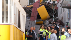 Investigadores da polícia (E) são fotografados ao lado de funcionários da empresa de transportes La Carris, de Lisboa, com os destroços do funicular da Glória ao fundo, um dia após o acidente que matou 15 pessoas em Lisboa, em 4 de setembro de 2025. Pelo menos 15 pessoas morreram e outras 18 ficaram feridas quando um famoso funicular descarrilou em Lisboa em 3 de setembro de 2025, segundo equipes de resgate. (Foto de PATRICIA DE MELO MOREIRA / AFP)