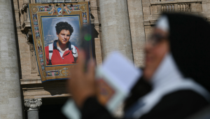 Uma freira verifica seu celular enquanto um retrato do falecido adolescente italiano Carlo Acutis é exibido na fachada da Basílica de São Pedro, ao fundo, antes da Santa Missa e da canonização do Beato Carlo Acutis e de Pier Giorgio Frassati na Praça de São Pedro, no Vaticano, em 7 de setembro de 2025. Um adolescente italiano apelidado de "Influenciador de Deus" por seus esforços para espalhar a fé católica online se tornará o primeiro santo milenar neste domingo, em uma canonização com a presença de milhares de peregrinos. O gênio da computação Carlo Acutis, que morreu de leucemia em 2006 aos 15 anos, será canonizado pelo Papa Leão XIV em uma cerimônia solene na Praça de São Pedro, no Vaticano. O italiano Pier Giorgio Frassati, um entusiasta do montanhismo que morreu em 1925 e era conhecido por seu compromisso social e espiritual, também será canonizado em 7 de setembro de 2025. (Foto de Filippo MONTEFORTE / AFP)