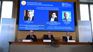 O Prêmio Nobel de Economia foi concedido ao americano-israelense Joel Mokyr, ao francês Philippe Aghion e ao canadense Peter Howitt por seus trabalhos sobre o impacto da tecnologia no crescimento econômico sustentado. Mokyr recebeu metade do prêmio "por ter identificado os pré-requisitos para o crescimento sustentado por meio do progresso tecnológico", enquanto Aghion e Howitt dividiram a outra metade "pela teoria do crescimento sustentado por meio da destruição criativa", afirmou o júri. Uma tela mostra (da esquerda para a direita) o americano-israelense Joel Mokyr, o economista francês Philippe Aghion e o canadense Peter Howitt enquanto o Secretário-Geral da Real Academia Sueca de Ciências, Hans Ellegren (do centro), se dirige a jornalistas, ladeado por membros do comitê do Prêmio Nobel de Economia (da esquerda para a direita) e Kerstin Enflo, durante o anúncio do vencedor do Prêmio Nobel de Economia de 2025, o Prêmio Sveriges Riksbank em Ciências Econômicas em Memória de Alfred Nobel, na Real Academia Sueca de Ciências, em Estocolmo, Suécia, em 13 de outubro de 2025.