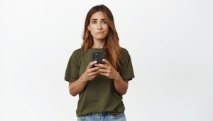 Mulher de meia-idade decepcionada e chateada segurando um smartphone, franzindo as sobrancelhas e sorrindo com cara triste